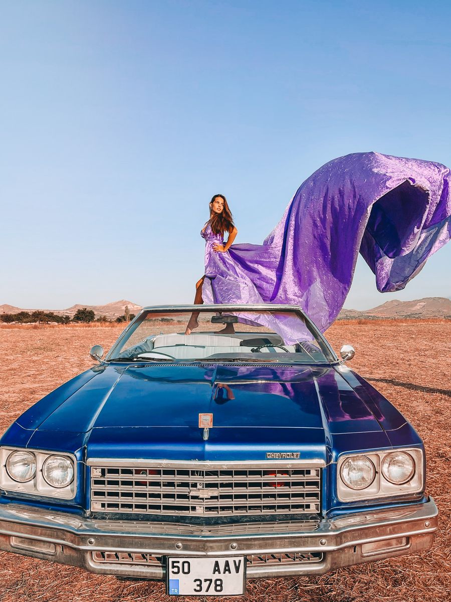Placeholder portrait of a woman in a flowing dress on a vintage car